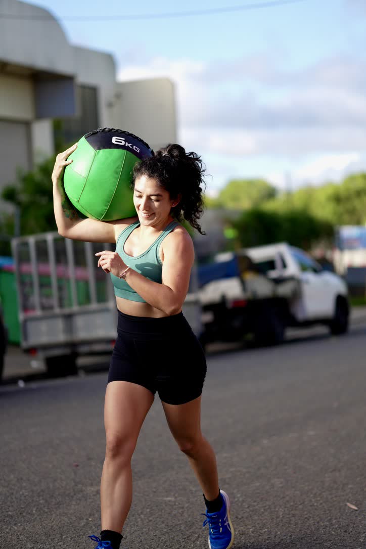 CrossFit Brisbane member carrying a green medicine ball outdoors